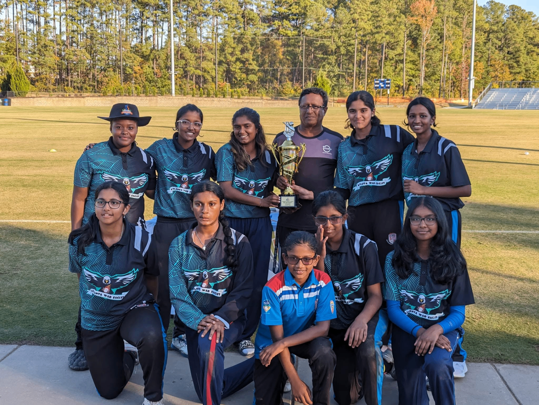 SN Cricket Academy players holding a championship trophy with Head Coach Sudhir Nair on the field in Georgia
